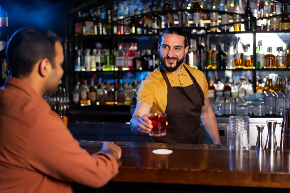 A professional bartender offers a drink to a customer, showcasing good bar service.