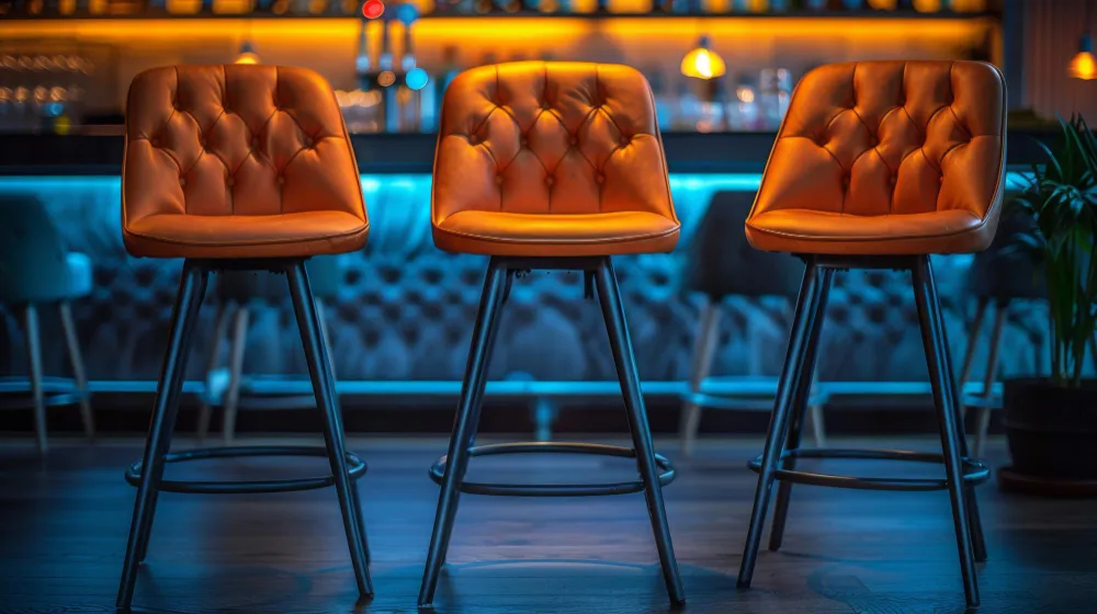 Close-up of ergonomic tufted leather bar stools with supportive backrests designed for long-stay customer comfort.